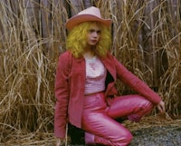 a woman in pink pants and a hat is crouching in a field