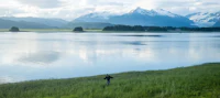 a person is standing in front of a lake with mountains in the background