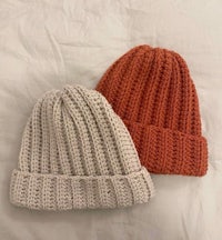 two knitted beanie hats on a bed