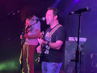 two men playing guitar on stage in front of a microphone