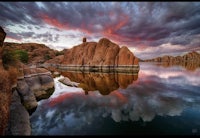 a sunset over a lake with rocks in the water