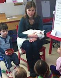 a woman is sitting in front of a group of children with a cat