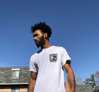 a man wearing a white t - shirt standing in front of a house