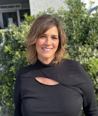 a woman in a black top smiling in front of bushes