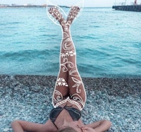 a woman laying on the beach with a mermaid tail tattoo