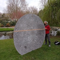 a man standing next to a large circular sculpture in a park
