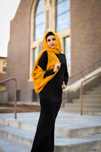 a woman in a black dress and yellow hijab posing on steps