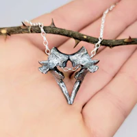 a hand holding a silver necklace with a heart on it