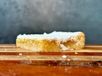 a slice of lemon bar with powdered sugar on a wooden cutting board