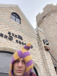 a man wearing a purple and yellow hat in front of a building