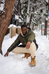 a man kneeling down in the snow next to a tree
