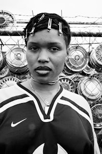 a woman in a black and white photo standing in front of a fence