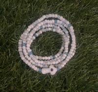 a white and blue beaded bracelet laying on the grass