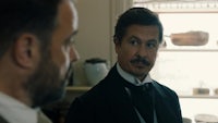 a man in a tuxedo is looking at a man in a suit