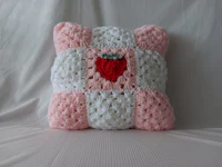 a pink and white crocheted pillow with a strawberry on it