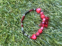 a red and black beaded bracelet laying on the grass