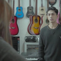 a man and a woman standing in front of a wall of guitars