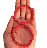 a person's hand holding two red bead bracelets