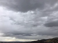 a cloudy sky over a city with mountains in the background