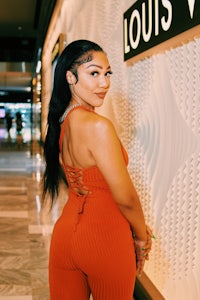 a woman in an orange jumpsuit posing in front of a louis vuitton store