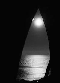 a black and white photo of the moon through an arch