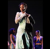 a woman in a dress on stage with other dancers
