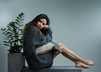 a woman in a gray sweater sits on a concrete block with a potted plant