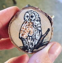 a person holding a piece of wood with an owl on it