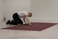 a man kneeling down on a red rug in an empty room
