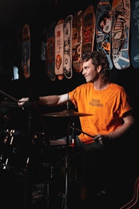 a man playing drums in front of a wall of skateboards