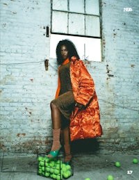 a woman in an orange coat standing next to a basket of tennis balls