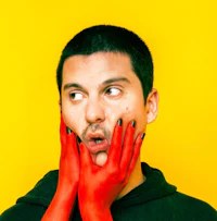 a man with red gloves covering his face on a yellow background