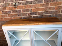 a white cabinet with glass doors in front of a brick wall