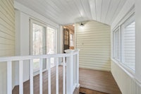 the front porch of a home has white walls and a railing