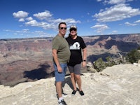 two people standing on a cliff overlooking the grand canyon