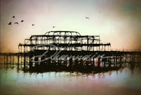 an image of a pier with birds flying over it
