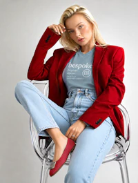 a woman wearing a red blazer and jeans sitting on a chair