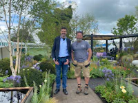 two men standing next to each other in a garden