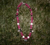 a pink and black beaded necklace laying on the grass