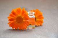 two orange flowers and a bottle of essential oil on a wooden table