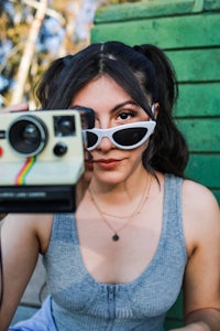 a woman wearing sunglasses holding a polaroid camera