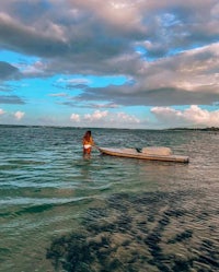 a woman in a bikini standing in the water with a surfboard