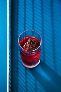 a glass of red liquid sitting on a blue surface