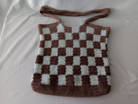 a brown and white crocheted bag on a bed