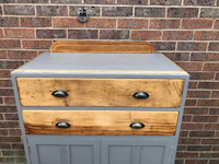 a gray dresser with wooden drawers in front of a brick wall