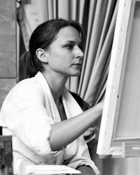 a black and white photo of a woman painting on an easel
