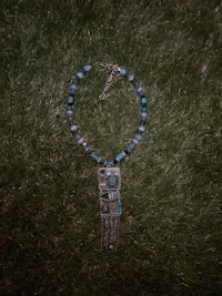 a blue and silver necklace laying on the grass