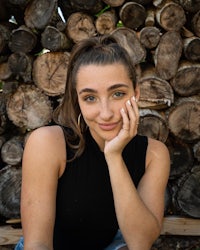a young woman posing in front of a pile of logs
