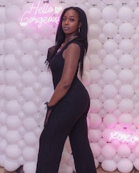 a woman in a black jumpsuit posing in front of a neon wall