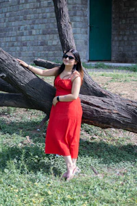 a woman in a red dress leaning against a tree